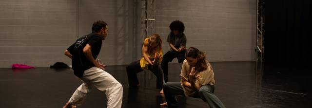 a man demonstrates a deep plie to three female dancers who mimic his movement