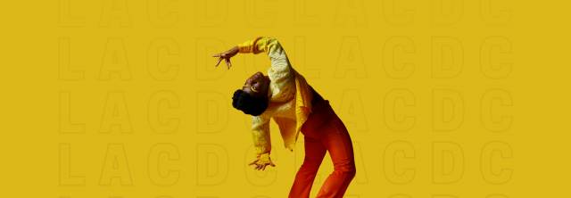 brown skinned dancer wearing ombre yellow top and orange pants bends over backwards looking beyond in a pose, fingers splayed above and below her head