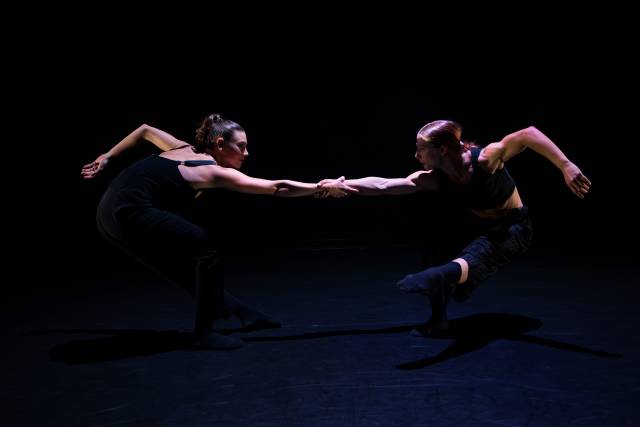 2 women counterbalance while holding each other's arm and standing on one leg