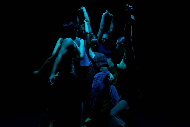 a group of bodies in blue with arms raised and undulating 