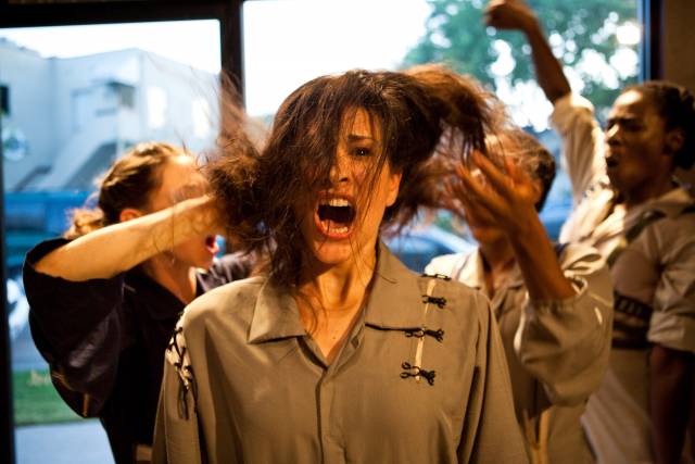 an olive skinned woman looks out in shock as people behind her rustle her hair