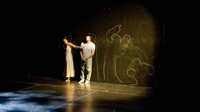 two figures up against a black wall with chalkboard figure drawings
