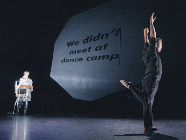 text projected onto a wall while a man stands on one leg with his arms raised