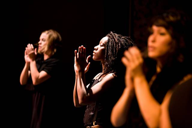 3 women, fair skinned, brown skinned, and medium skinned, wearing black, clap their hands