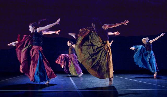 a group of women wearing long skirts throw their arms back and their leg up