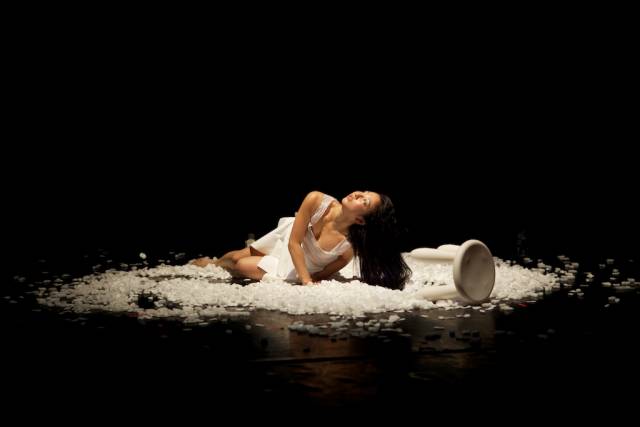 a woman wearing white lays on the floor on top of styrofoam, looking upward