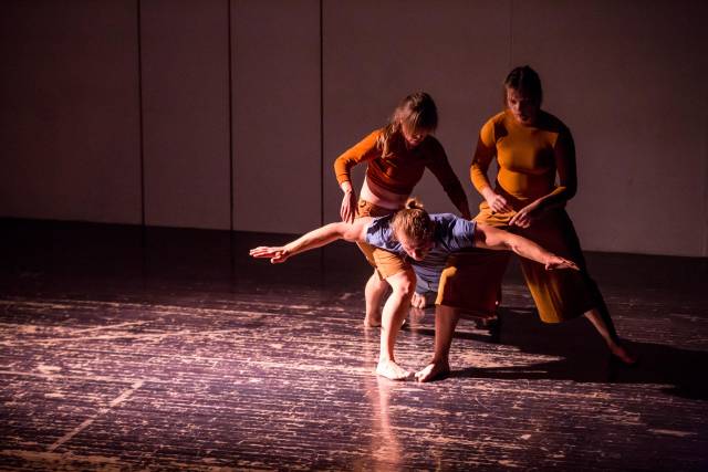 a man balances his chest on the knees of two women