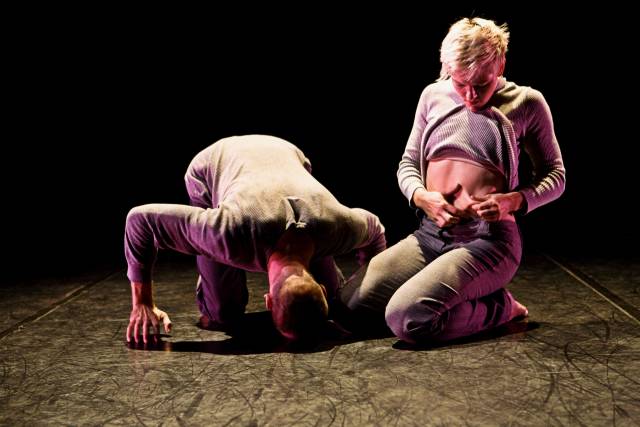 a man touches his head to the floor while a woman pulls at her belly