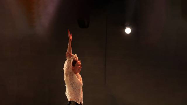 a fair skinned woman raises her hand while smiling