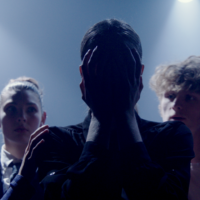 a figure stands in silhouette with hands on their face as four concerned looking figure stand behind them