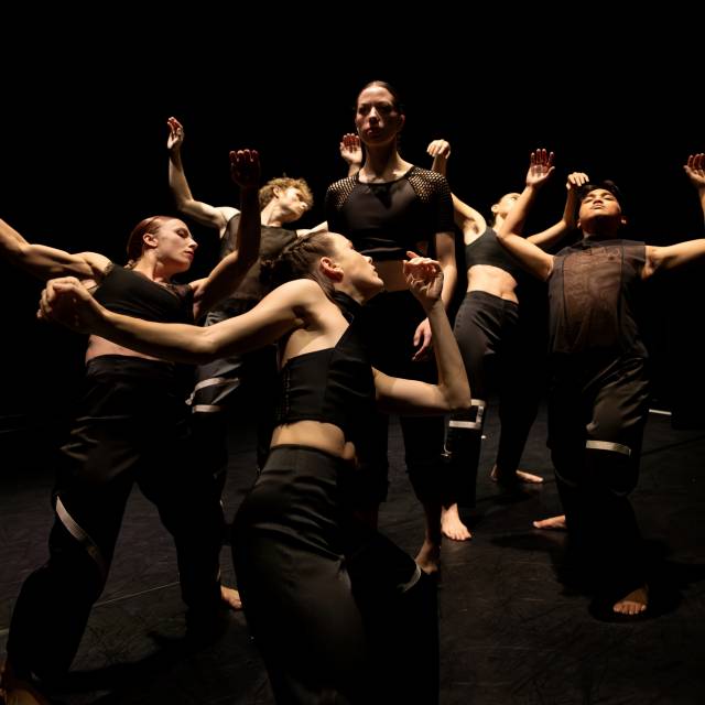 a person looks out into the distance while being surrounded by a group of five bodies with arms flailed backwards