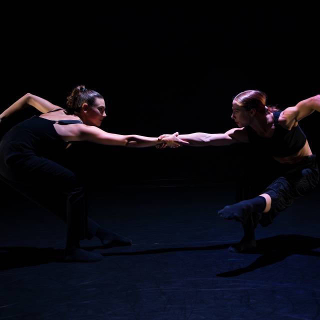 2 women counterbalance while holding each other's arm and standing on one leg