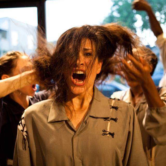 an olive skinned woman looks out in shock as people behind her rustle her hair