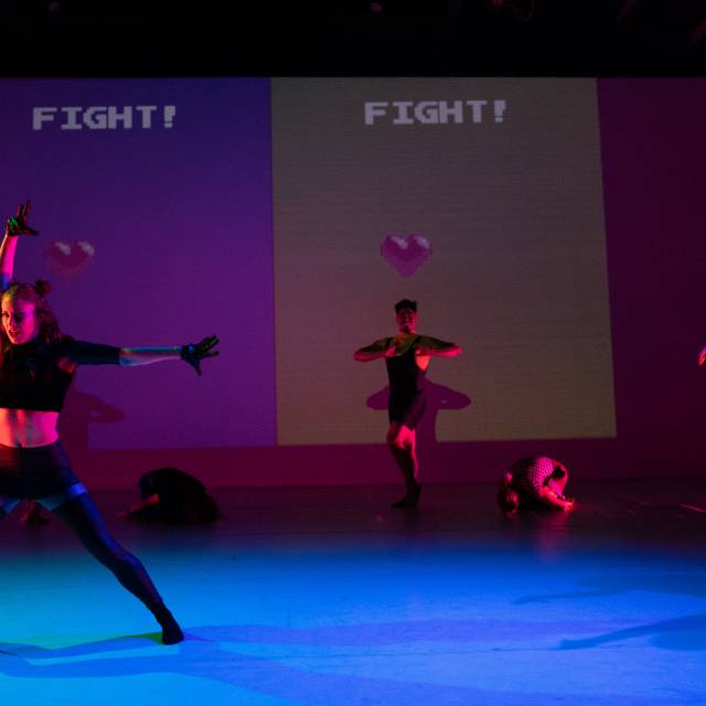 two figures pose while a projection behind them shows the words "FIGHT"