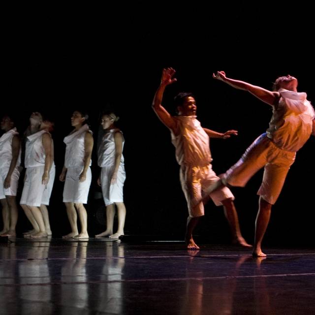 two figures in white dance while a group of figures in white are in the background