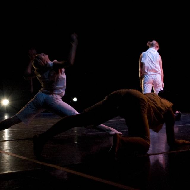 a figure wearing white hovers in a split with her arms thrown up in the air