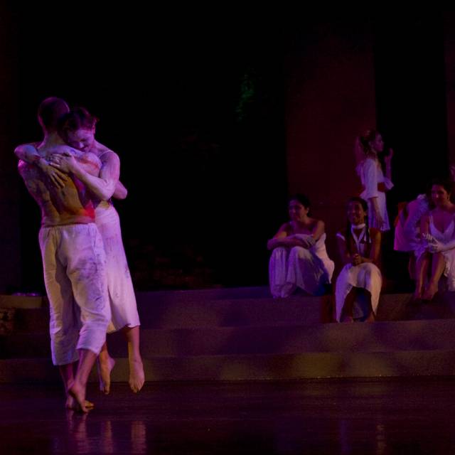 two figures painted in white hug while a group of people watch