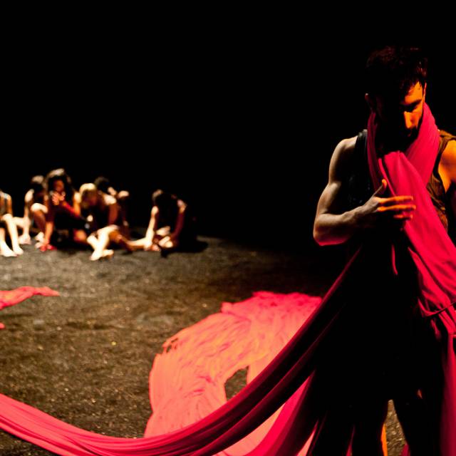 a man wrapped in a red cloth while a group of people sit on the ground in the background