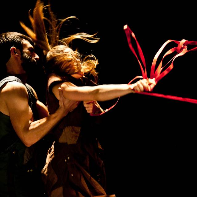 a woman holds on to a red rope while thrashing her head. a man holds onto her arm.