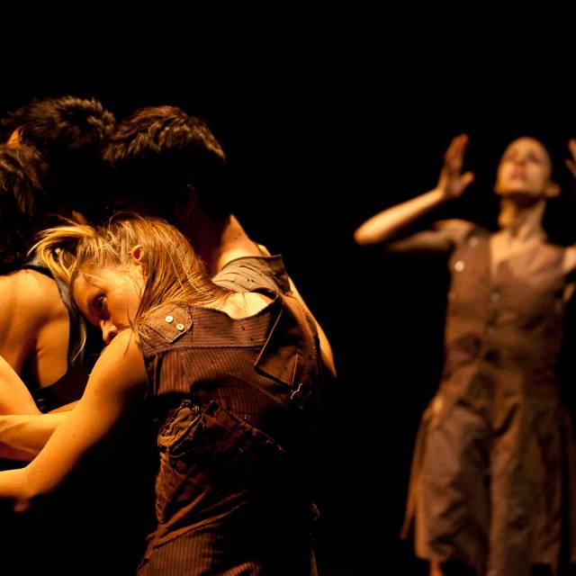 a group hug with person standing in the background with their hands framing their face