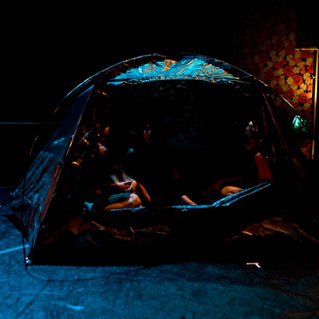 several figures sitting in a black in tent