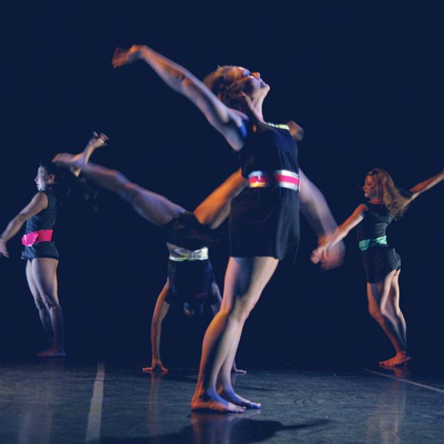 three women throw their arm back while another woman is in mid-cartwheel