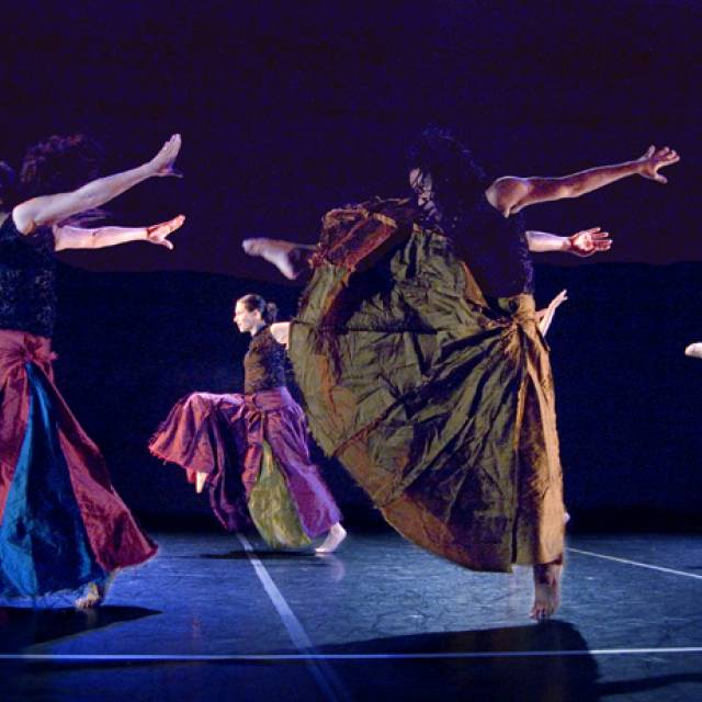 a group of women wearing long skirts throw their arms back and their leg up