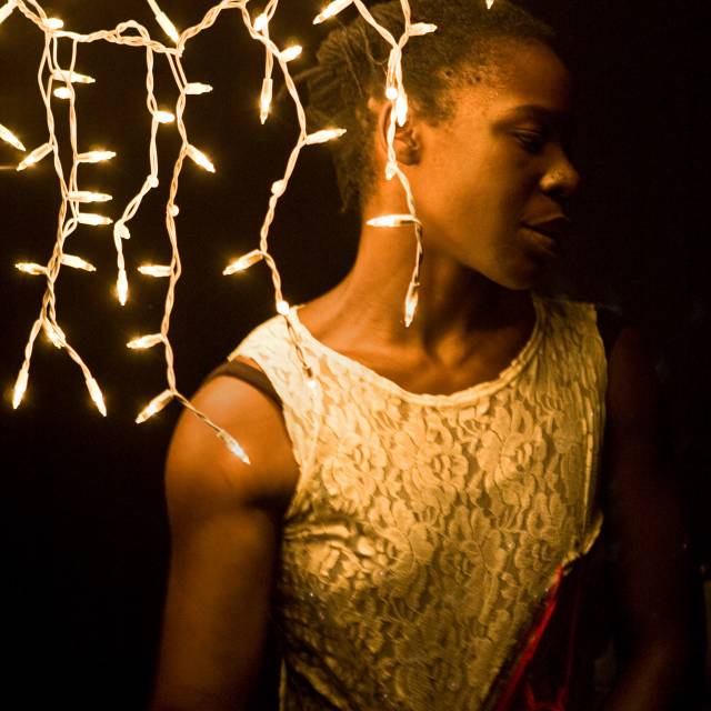 A brown skinned woman stands under hanging christmas lights