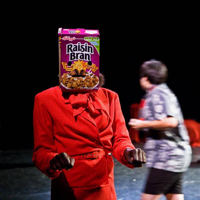 a figure stands with a cereal box on their head