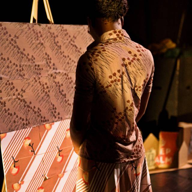 a woman stares at artwork on an easel that matches her outfit exactly