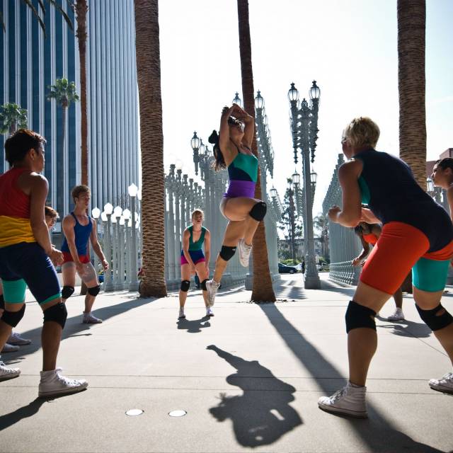 woman wearing brightly colored outfit jumps in the middle of a circle of people wearing the same