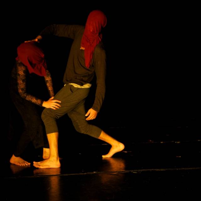 two people partner each other, both faces covered by maroon cloth