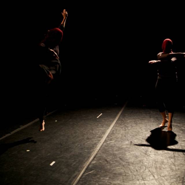 a person jumps next to another, both faces covered with maroon cloth