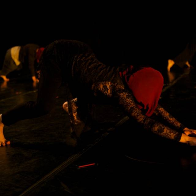 a person crawls on the ground, face covered by a maroon cloth
