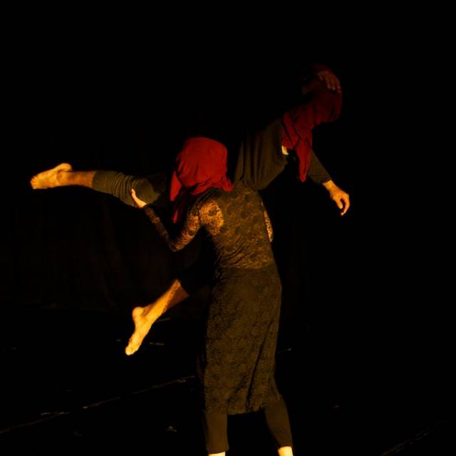 one person lifts another, both their faces covered in maroon cloth