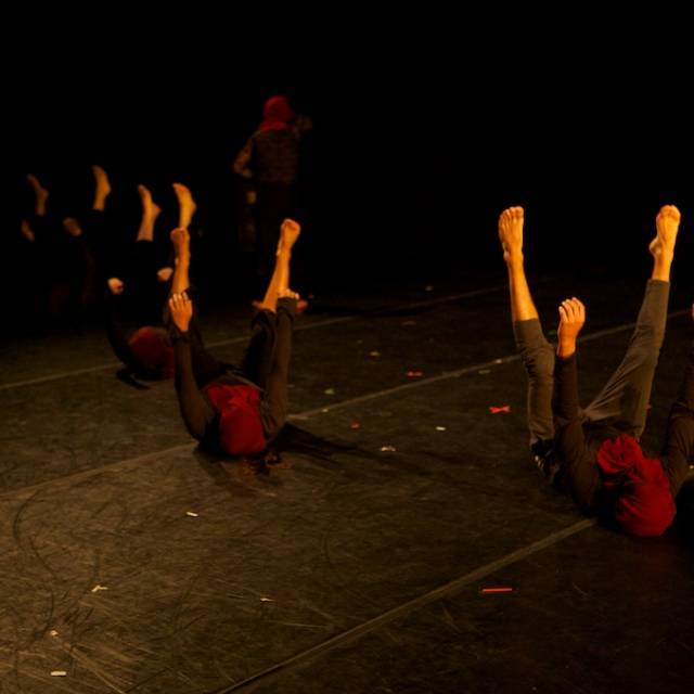 four people laying on the floor with their legs and arms hovering in the air, their faces covered with a maroon cloth