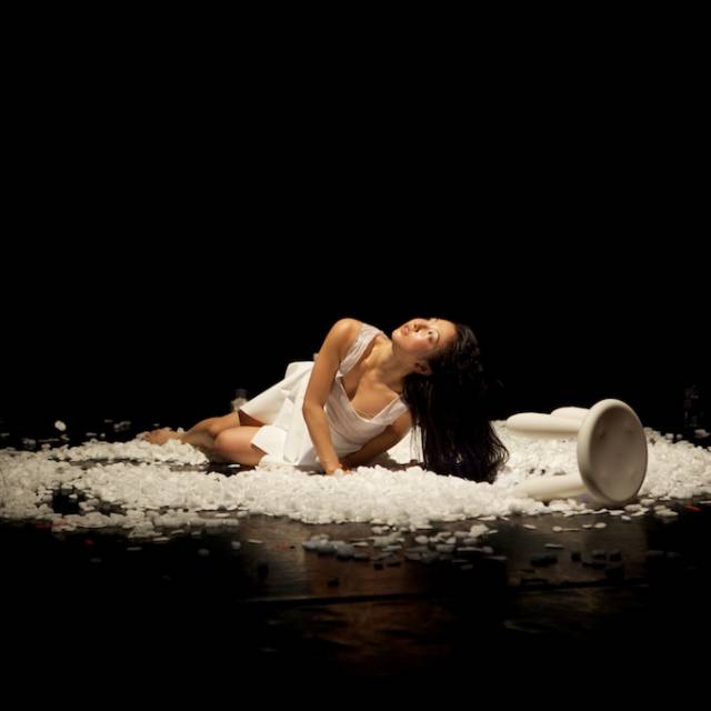 a woman wearing white lays on the floor on top of styrofoam, looking upward