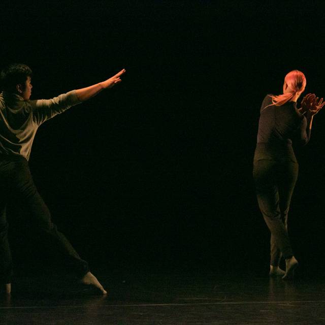 a man reaches out one arm and one leg while a woman walks upstage