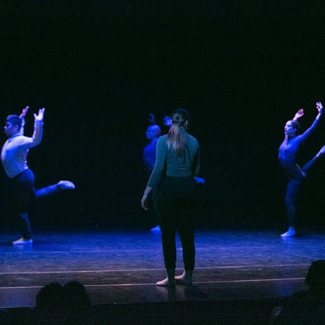 a woman watches three dancers who stand in attitude