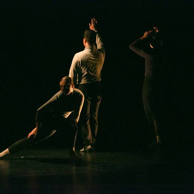 a woman in a lunge while two dancers face upstage with one arm raised