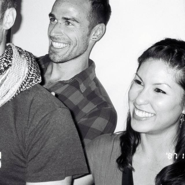 two men and one woman with big smiles look offscreen