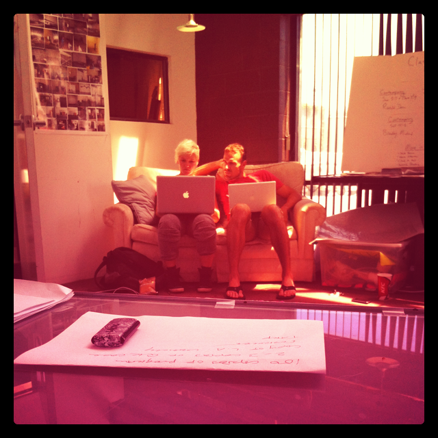 a man and woman sit on a couch with their laptops