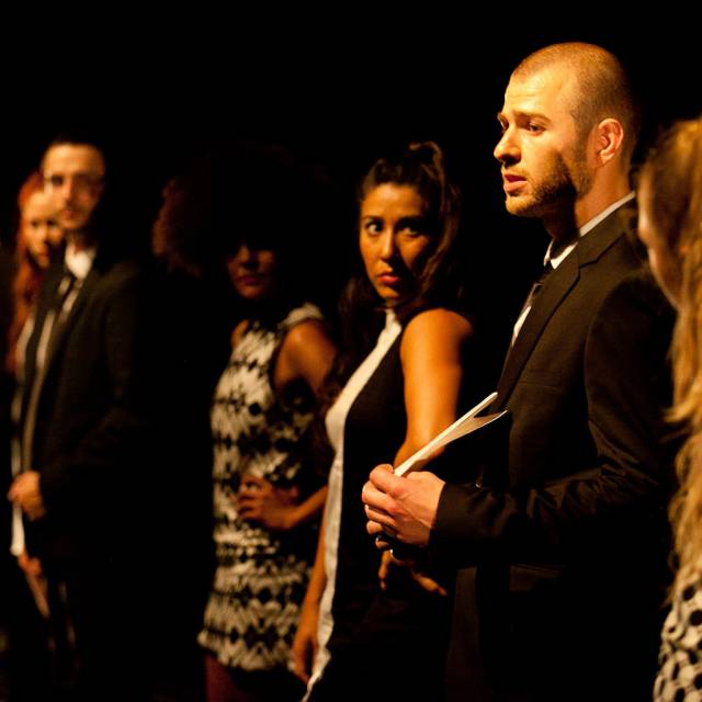 a group of people watch a man speak while he holds a letter