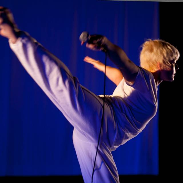 a woman in arabesque with arms thrown back while holding a microphone in one hand