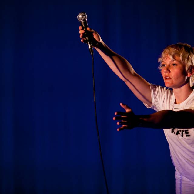 a woman in profile holding a microphone stretches her arms outward