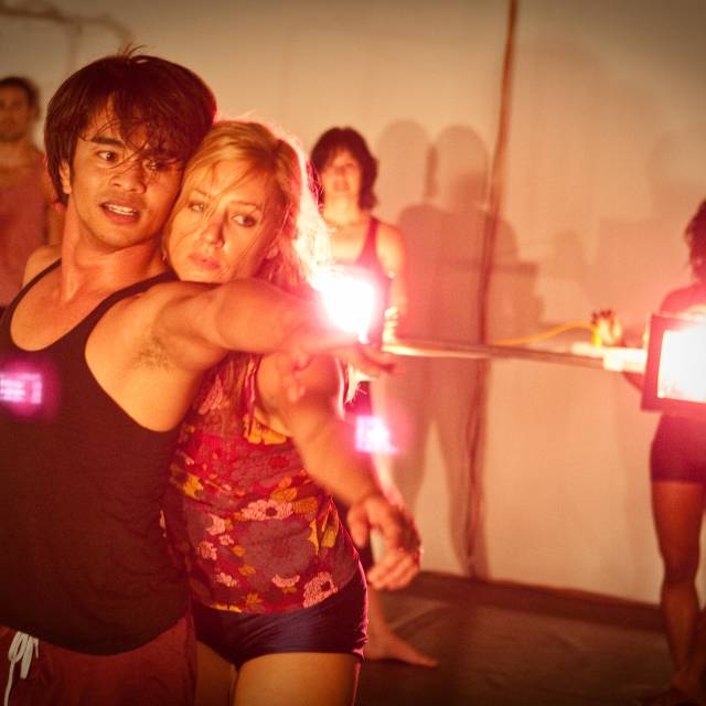 a woman stands behind a man resting her had on his shoulder as they both extend an arm