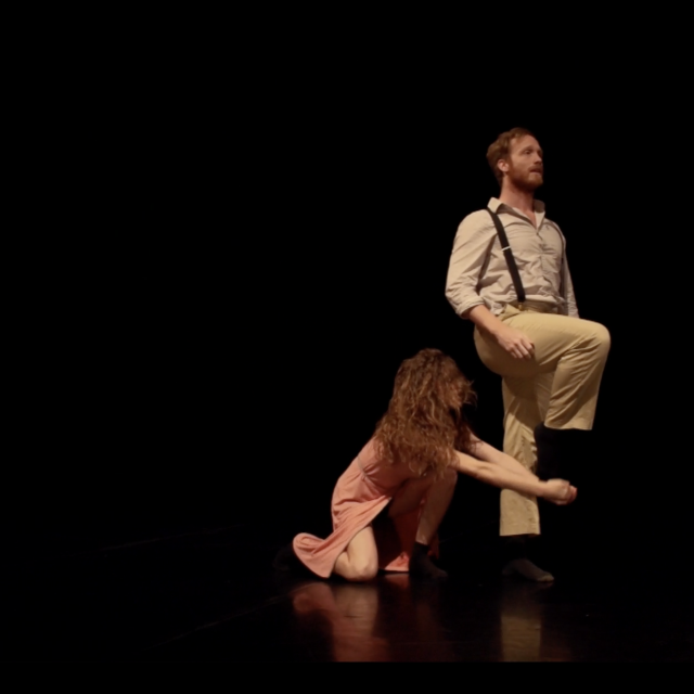 a man balances on one leg while a woman on the ground tries to capture his foot