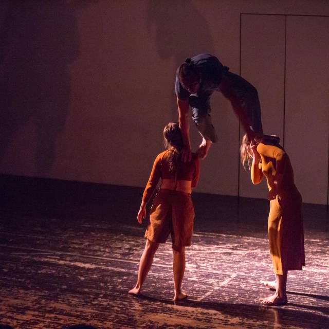 a man climbs on the shoulders of two women