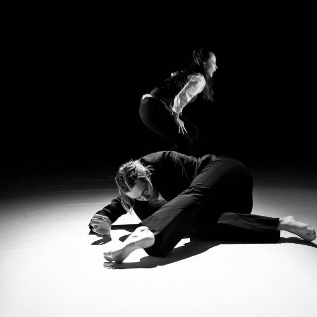 a woman extends her leg on the floor. another woman crouches behind her.