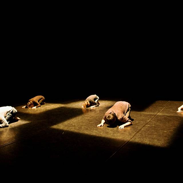 5 figures kneel with their heads pressed to the floor. each figure is in a square spotlight. 